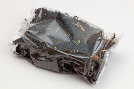 Black tea packaging on a white background. Long leaf tea with rose hips, apples and flower petals, packed in a transparent package. Tea with a fruity aroma. Isolated. Tea Packaging Concept. Close-upの写真素材