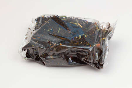 Black tea packaging on a white background. Long leaf tea with rose hips, apples and flower petals, packed in a transparent package. Tea with a fruity aroma. Isolated. Tea Packaging Concept. Close-upの写真素材