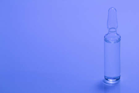 Medical ampoule on a blue background. Glass ampoule for injection with medicine on the table. Concept medicines and disease treatment. Pharmacology, cosmetology, science. Copy space for text. Close-upの写真素材