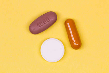 Multi-colored pills on a yellow background. Colorful medicines of different shapes on a bright...