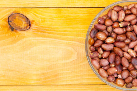 Roasted peanuts in a cup with copy space for text and advertising. Nut peanuts in a peel in a transparent bowl on a wooden textured table. The best snack for beer. Banner for bars and pubs. Close-upの写真素材