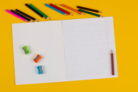 School notebook on a yellow background with copy space text, colorful pencils, pencil sharpeners. Back to school. Blank sheet of paper with oblique lines in exercise book. School Sの写真素材
