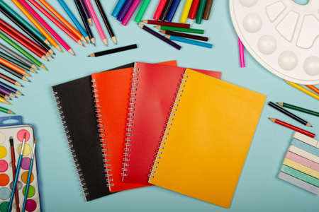 Multicolored notebooks, black, red and orange, art school supplies for painting, on a blue...