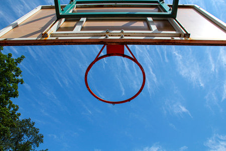 Basketball ring on the background a blue sky with white clouds and green tree. Basketball hoop on a shield on an outdoor sports ground. Basketball equipment. Copy spaceの写真素材