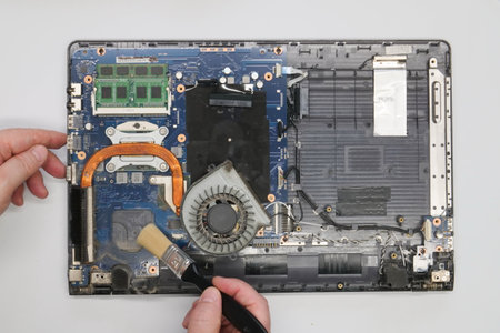Repairman cleaning a disassembled laptop on a white background. Isolated. Dusty computer repaired in a service workshop. Computer motherboard, chips, fan, wires, connectorsの写真素材