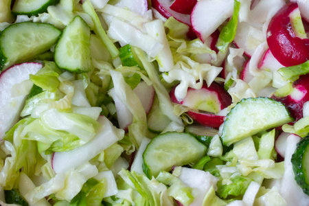 Mixing vegetable salad. Vegetarian salad of radish, cucumbers, cabbage, salt, olive oil. Healthy food. Salad of ripe chopped vegetables is mixed with a fork. Fresh vegetablesの写真素材