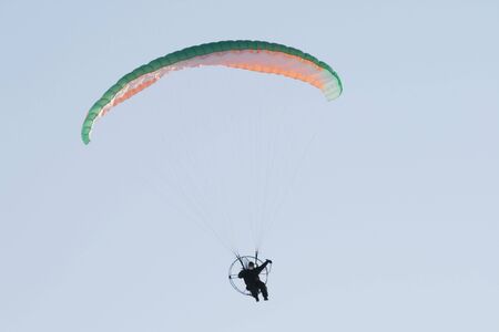 A multi-colored parachute holds up this paraplane on a clear blue day.の写真素材