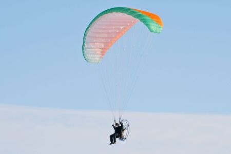 A multi-colored parachute holds up this paraplane on a clear blue day.