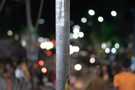 Dirty street pole with stickers and markings in a busy Indian market street at night with bokeh background, city nightlifeの写真素材