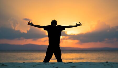 Silhouette of a man with open arms during sunset in a beach, relaxing life during vacationの写真素材