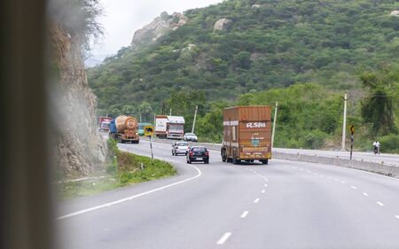 Krishnagiri, Tamil Nadu / India - 9th August 2019: Private and commercial vehicles moving up between two hills in a six lane national highway in india, efficient and safe land transportationのeditorial素材