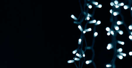 Soft abstract bokeh background. Dark copy space in left half to add text. Blurry Luminous garlands of electric lights. The gentle tone blue. Dark night. Festive party. Christmas. New Year.の写真素材