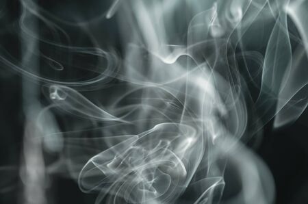 Thick, scenic clouds of smoke. From incense, or cigarettes, or cigars. Indoors. In the rays of sunshine on a dark background. Psychedelic mood. Close up. Colorful abstract background.の写真素材