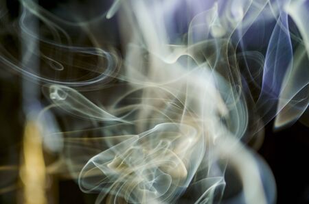 Thick, scenic clouds of smoke. From incense, or cigarettes, or cigars. Indoors. In the rays of sunshine on a dark background. Psychedelic mood. Close up. Colorful abstract background.の写真素材