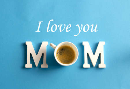 Happy Mother's Day. Mom lettering and cup of coffee on blue background. Flat and top view.