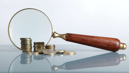 Closeup view of a magnifying glass looking at a stack of coins の写真素材