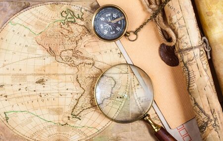 compass, magnifying glass and pen lying on an ancient world map
