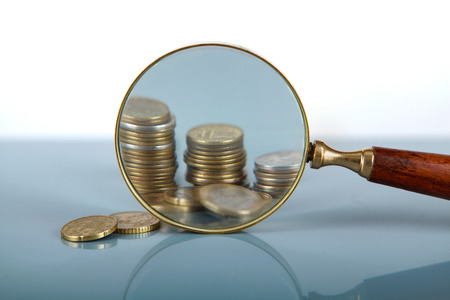 Closeup view of a magnifying glass looking at a stack of coinsの写真素材