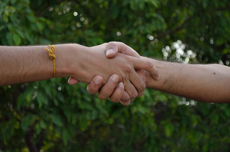 Two bare hands shaking hand on green background