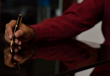 Human hand holding a pen on table along itの写真素材