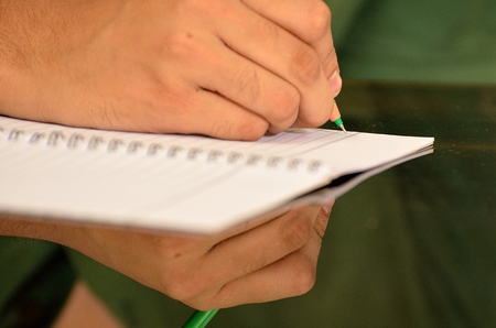 Human hand writing on notebook with a pen reflected on tableの写真素材