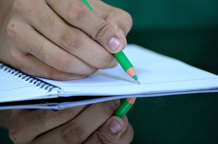Human hand writing on notebook with a green pen reflected on table