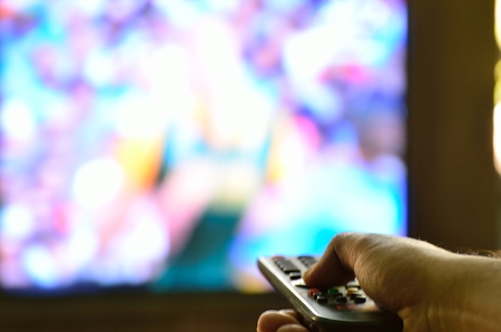 Shot of hand holding TV remote control in front television.
