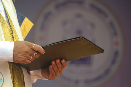 A human hand is offering a degree certificate during a convocation ceremony.