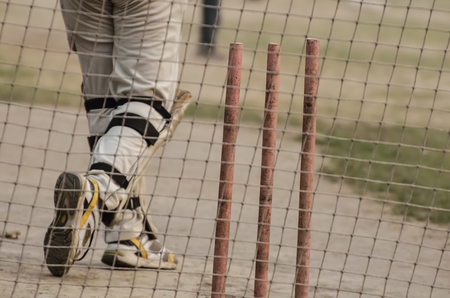 Boy is practicing cricket batting in net.