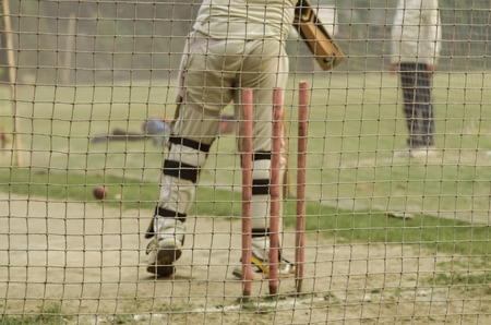 Boy is practicing cricket batting in net.