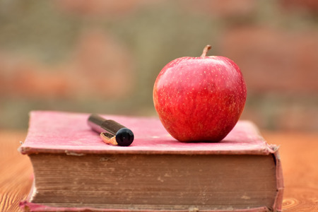 Old vintage books and red apple on wooden table and old brick wallの写真素材