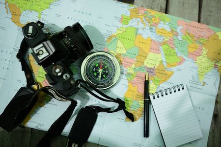 Analog camera, word map, notepad, pen and compass on wooden backgroundの写真素材