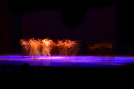 A group of people dancing on stage against dark black