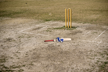 Cricket bat and gloves are on empty cricket pitch to play.
