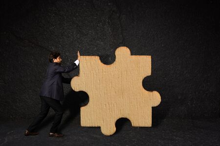 A businessman pushing a piece of puzzle as a business strategy against texture wall