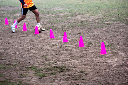 Footballer dribbling ball during training between cones. Young soccer players practicing dribblingの写真素材