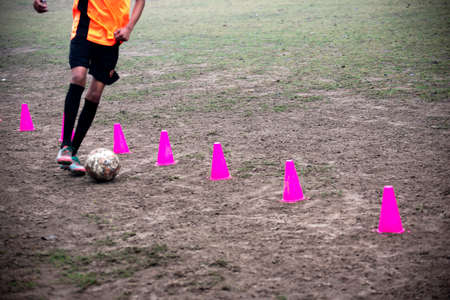 Footballer dribbling ball during training between cones. Young soccer players practicing dribblingの写真素材