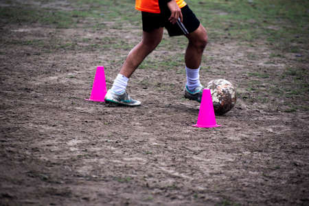 Footballer dribbling ball during training between cones. Young soccer players practicing dribbling.の写真素材