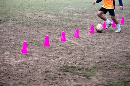 Footballer dribbling ball during training between cones. Young soccer players practicing dribblingの写真素材