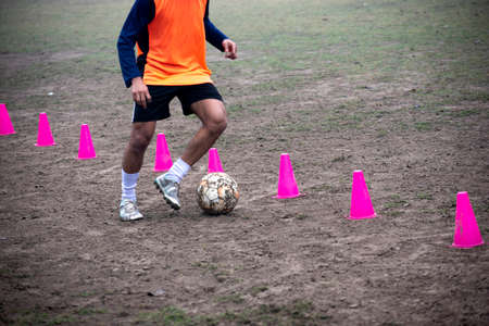 Footballer dribbling ball during training between cones. Young soccer players practicing dribblingの写真素材
