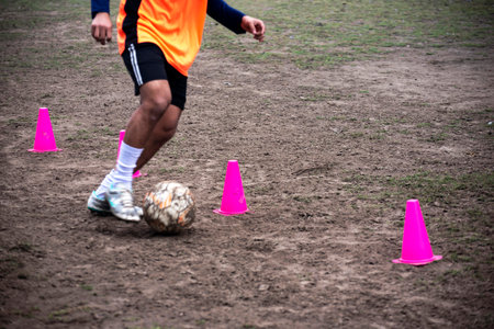 Footballer dribbling ball during training between cones. Young soccer players practicing dribblingの写真素材