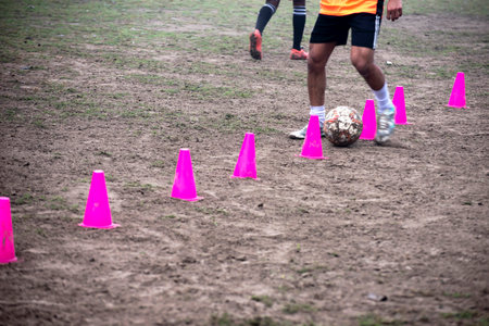 Footballer dribbling ball during training between cones. Young soccer players practicing dribblingの写真素材