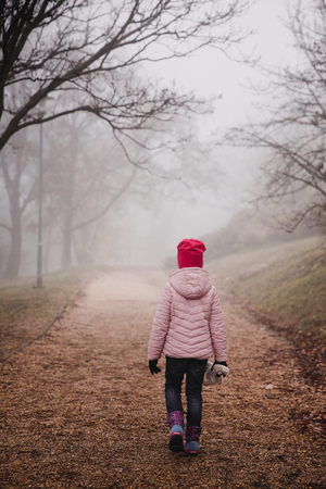 Girl in a pink jacket walking in an autumn misty forest in parkの写真素材