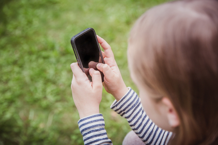 Cute little girl is using the smart phone. grass on background.の写真素材