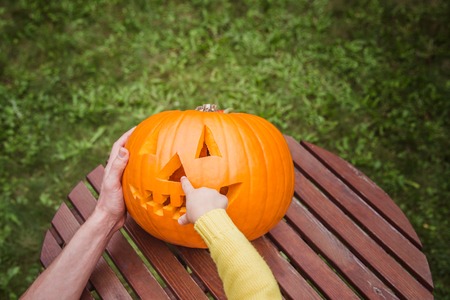 Happy halloween. Father and small daughters look at the face cut in the pumpkin high angle view. Small giirl show a nose of pumpkin Jack O Lanterns. Outside.の写真素材