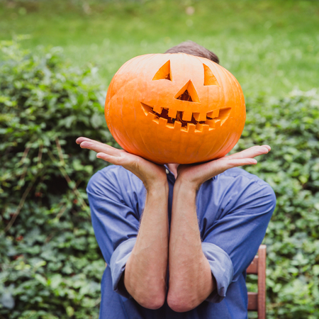 Man in blue shirt holding big pumpkin in front of his face. Happy Halloweenの写真素材