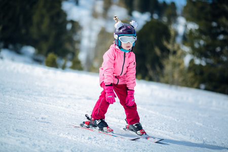 Little girl in pink ski costume skiing in downhill slope. Winter sport recreational activityの写真素材