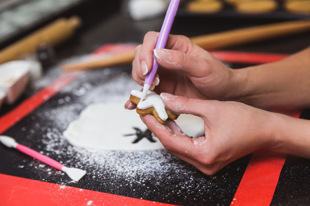 Woman decorates christmas gingerbread cookies with icing sugar glaze snowflake. Christmas gift, homemade and home painter gingerbread. Hands, close-upの写真素材