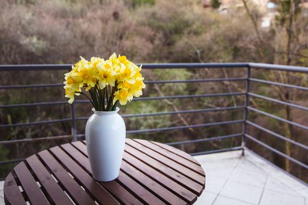Bouquet of yellow daffodils in a white vase on a wooden table outdoor. Close-upの写真素材