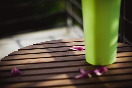Petals of a pink tulip lies on a wooden table near green vase on sun. Close-upの写真素材